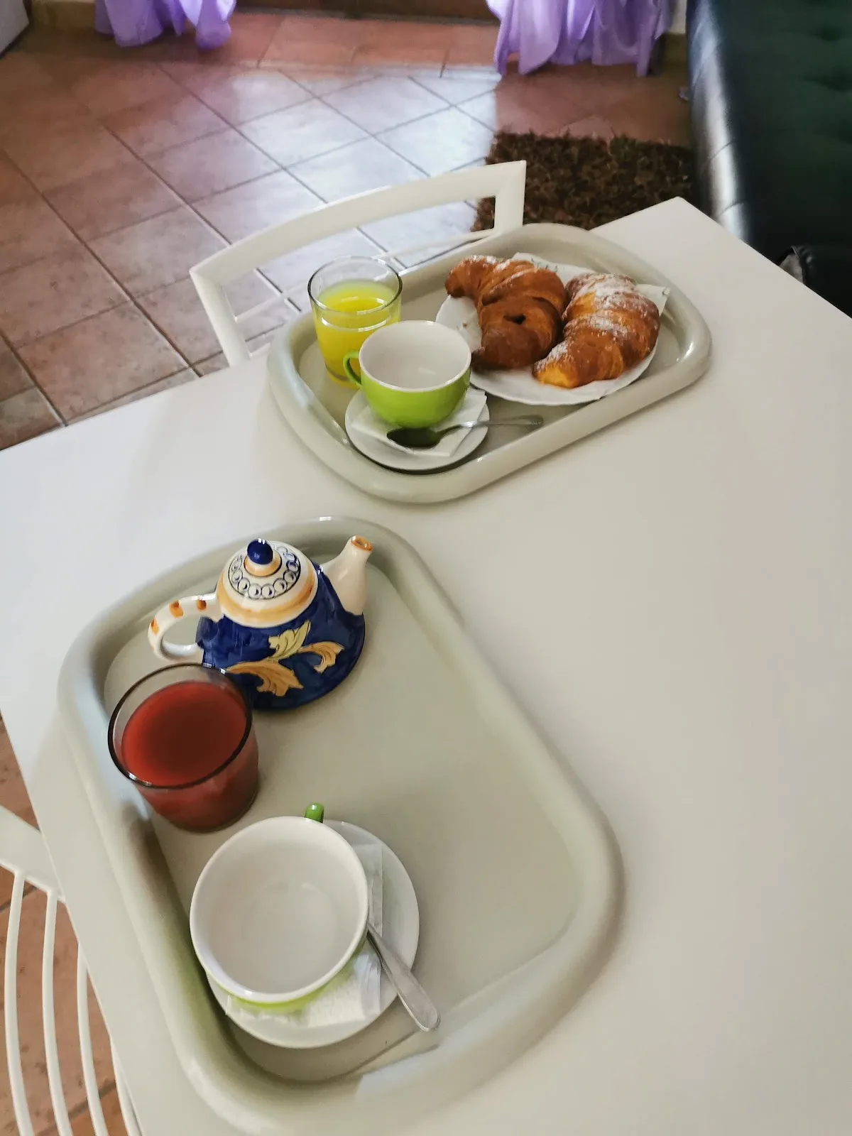Colazione servita con cornetti, spremuta d'arancia, tè e succo, su vassoi bianchi