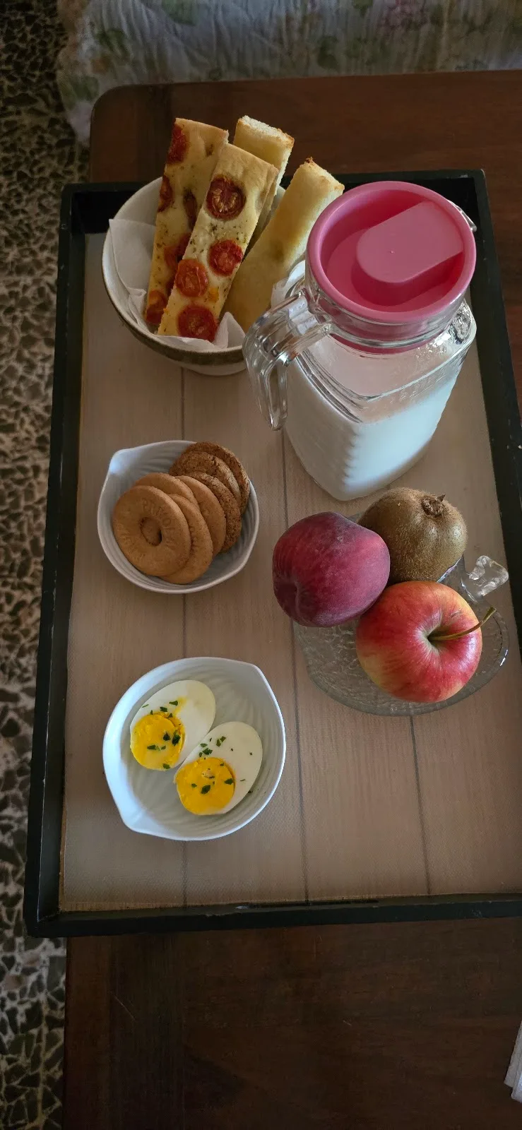 Vassoio della colazione con focaccia ai pomodorini, biscotti, uova, frutta fresca e latte